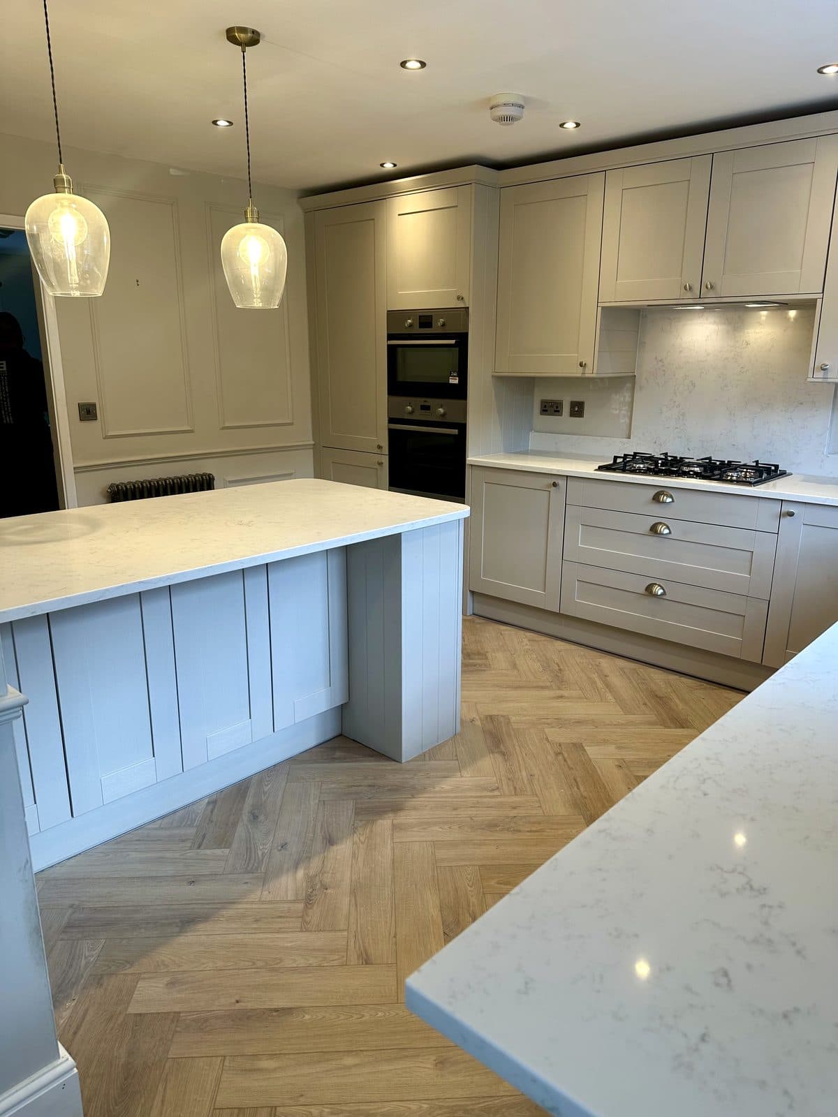 Shaker kitchen by Renovations of Cheshire, with quartz worktops, glass pendants and herringbone flooring